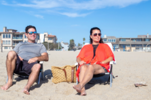 couple sitting in beach chairs on sandy beach wearing sunglasses
