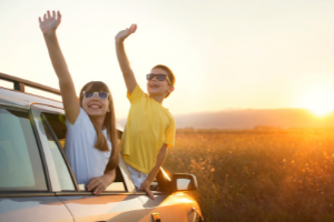Kids waving out of parked car wearing sunglasses