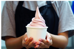 person in apron holding cup of pink frozen yogurt