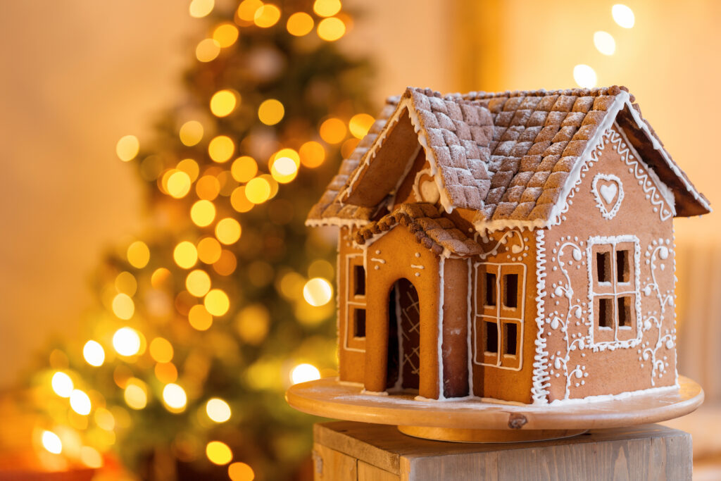 gingerbread house over defocused lights of Chrismtas decorated fir tree. Christmas eve, warm atmospheric light